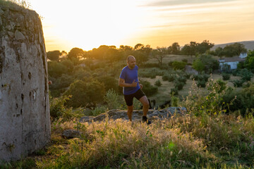 Middle-aged, bald trail runner sprinting at sunset, embodying determination and vitality.