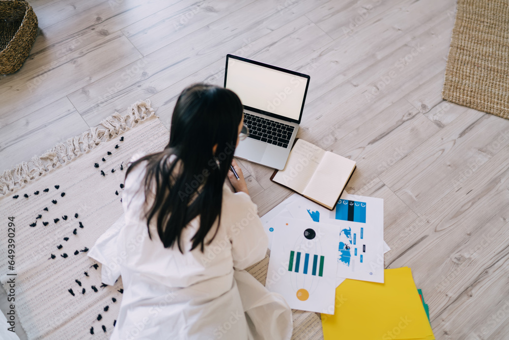 Poster female freelancer using laptop lying on floor with notebook and documents