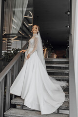 a full-length bride in a fashionable wedding dress stands on the steps of a restaurant and poses for a photographer. Wedding day. The best event