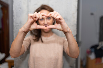 40 year old woman making a heart with her hands in front at home. homey feeling