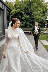 Naklejka premium The bride in a beautiful and fashionable dress in the foreground. The groom in a black suit goes to the bride