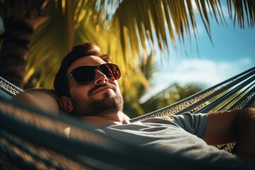 A man is seen laying in a hammock, wearing sunglasses and enjoying a moment of relaxation. This image can be used to depict leisure, vacation, or a peaceful lifestyle. - Powered by Adobe
