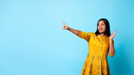 Excited Indian Lady In Dress Pointing Finger Aside, Blue Background