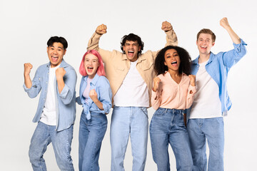 Overjoyed teen multiracial friends shouting and shaking fists, posing looking at camera, standing over white background