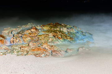 Colourful night long exposure of waves crashing against a rock on Patong Beach Phuket Thailand 