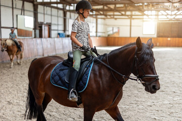 Horse riding school. Little children girls at group training equestrian lessons in indoor ranch...