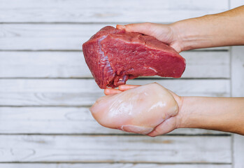 The girl holds in her hands large pieces of raw meat of beef and chicken on a wooden background....