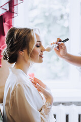 Girl make-up artist professional makes makeup on the face of a beautiful bride in the morning in a...