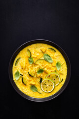 Curry soup with chicken meat, zucchini and chow mein  noodles on black background