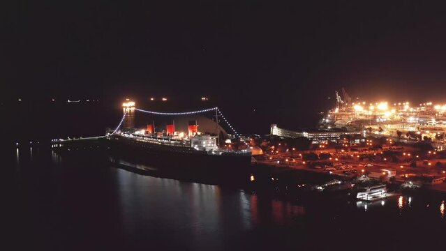 Queen Mary II flyover in Long Beach at night. The ship and the city in the background are lit up.