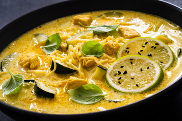 Curry soup with chicken meat, zucchini and chow mein  noodles on black background