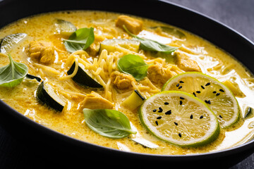 Curry soup with chicken meat, zucchini and chow mein  noodles on black background