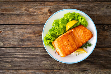 Seared salmon steak with lettuce and lemons on wooden table
