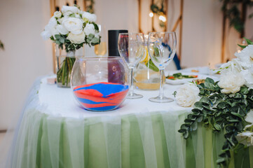 A glass bowl with colored, multi-colored sand is on the table. Wedding photography, decor, design.