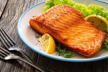 Seared salmon steak with lettuce and lemons on wooden table
