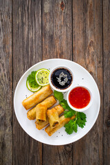 Vegetable filled spring rolls and sauces on wooden table
