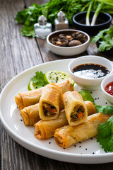 Vegetable filled spring rolls and sauces on wooden table
