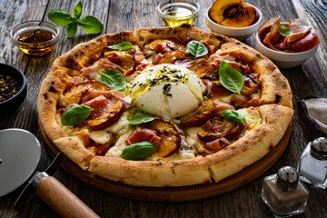 Circle prosciutto burrata pizza with grilled peaches on wooden table
