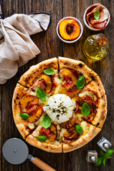 Circle prosciutto burrata pizza with grilled peaches on wooden table
