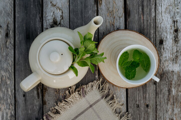 Top view of a teapot and tea cup with homemade lemon balm tea on a wooden table.