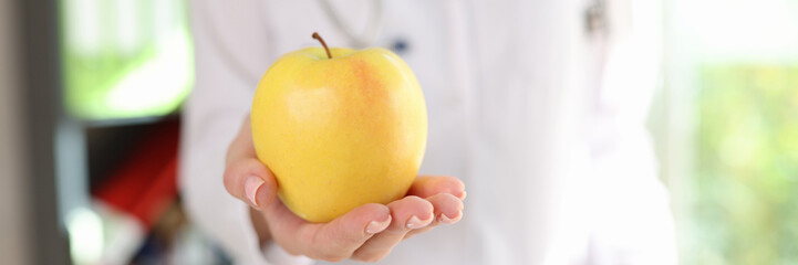 Ripe yellow apple in hand of female nutritionist, healthy eating concept.