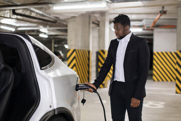 Confident entrepreneur plugging in charging cable into battery-powered car's port before leaving...