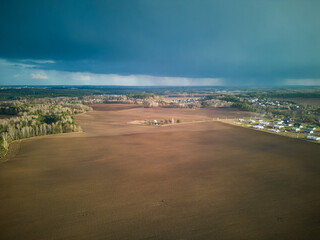 Aerial view over a small village near a dirt road. Large multi-colored fields planted with various agricultural crops. Wheat field from a bird's-eye view.