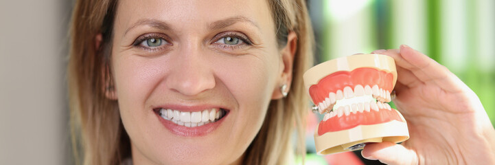 Smiling woman dentist shows jaws with artificial teeth close up.