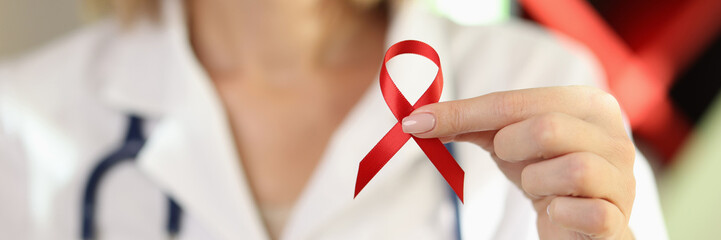 Woman doctor holding red ribbon as symbol of AIDS close up. - obrazy, fototapety, plakaty