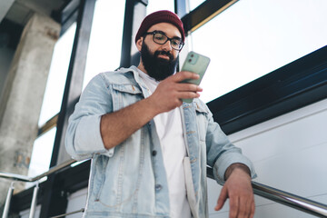 Concentrated young bearded man chatting on mobile phone standing near window