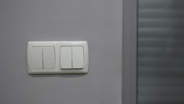 A man turns on and off the light in the room. Two double switches on a gray wall. Looping endless video.