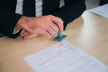 Businessman hand stamping an approved stamp on a text document at a table with a contract form...