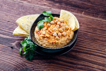 Traditional Indian chickpeas dip with pita bread and herbs as close-up in a design bowl with copy...