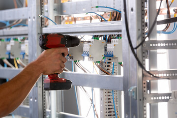 A male electrician works in a switchboard with an electrical connecting cable.