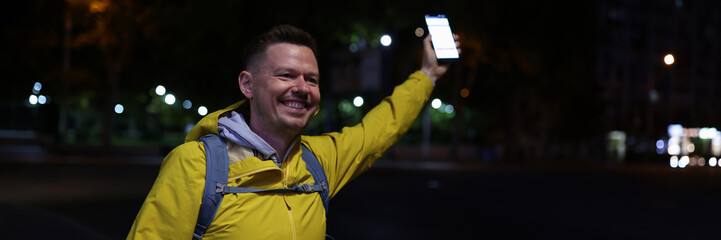Smiling man holds cellphone in his hand and welcoming friend in evening street.