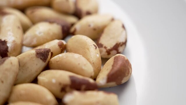 Brazil nuts heap on a white ceramic surface. Vegan, vegetarian nutritious food concept. Rotation
