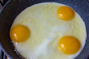 Three chicken eggs are fried in a pan