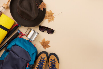 Must-have items for an autumn hike. Top view arrangement of camping equipment, hat, eyewear, fallen leaves on pastel brown background with advertising zone
