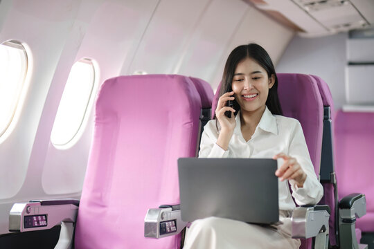 Asian woman using modern smartphone and laptop computer while sitting on airplane Asian woman sitting next to airplane seat window travel and technology