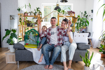 traditional family with a child and a parrot pet in a cage are enjoying a new home, sitting on the sofa and holding the roof. Mortgage, insurance, buying and moving into your own home