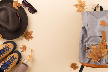 Inspiring autumn adventure ideas. Top view flat lay of woolen hat, grey rucksack, sunglasses, footwear, water bottle, fallen leaves on pastel brown background with ad area