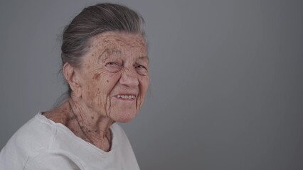 Senior woman 90 years old smiles, laughs and shows a denture on a gray background. Elderly female with deep wrinkles and gray hair happy in a good mood studio portrait looking at camera.