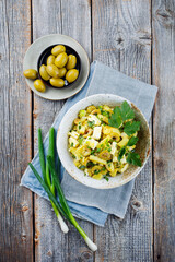 Traditioneller griechischer Kartoffelsalat mit Schafskäse und Oliven serviert als Draufsicht in einer Design Schale auf einem rustikalen Holz Board mit Textfreiraum