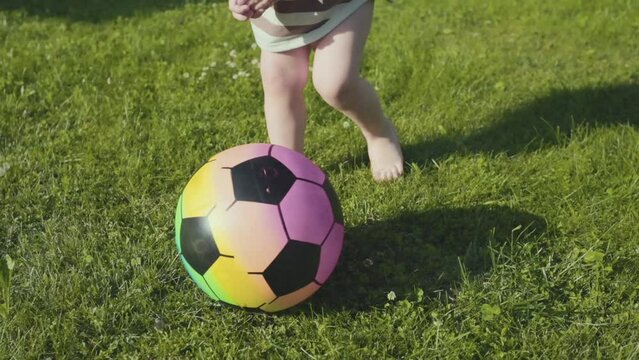 a little boy runs barefoot on the green grass and kicks a ball, first steps