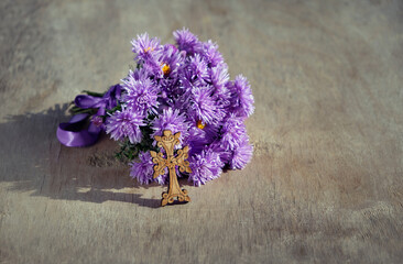 Wooden christian cross with violet Michaelmas daisies flowers close up on abstract wooden...