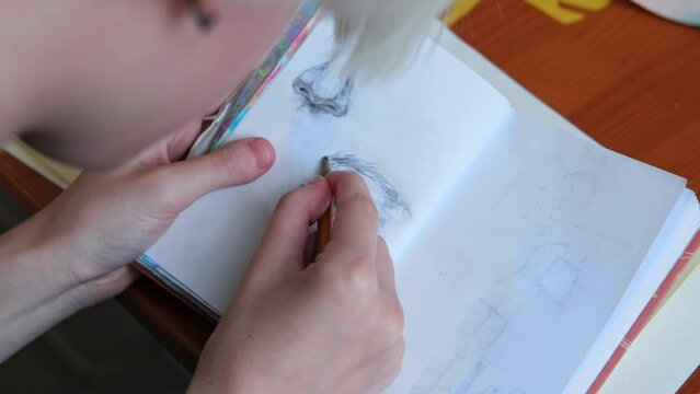 Artist draws an eye with a pencil in sketchbook. Elements of drawings close-up.
