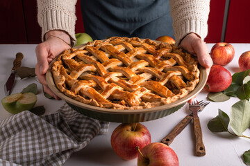 Woman holding and showing tasty cooked apple pie ready to be putting in the oven. Thanksgiving tart preparation, autumn bakery. Crispy weather sweets. Recipe - obrazy, fototapety, plakaty