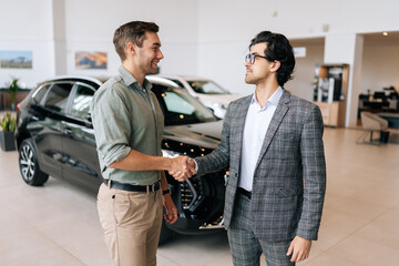 Portrait of professional salesman in business suit shaking happy client hand and talking. Stylish...