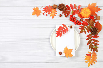 Autumn abstract composition with maple leaves, pumpkins and rowan berries, still life, blank white card on plate for menu layout, Thanksgiving concept, seasonal background, banner or screensaver, 