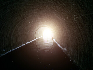 Light at end of round flooded sewer tunnel. Exit from sewer system